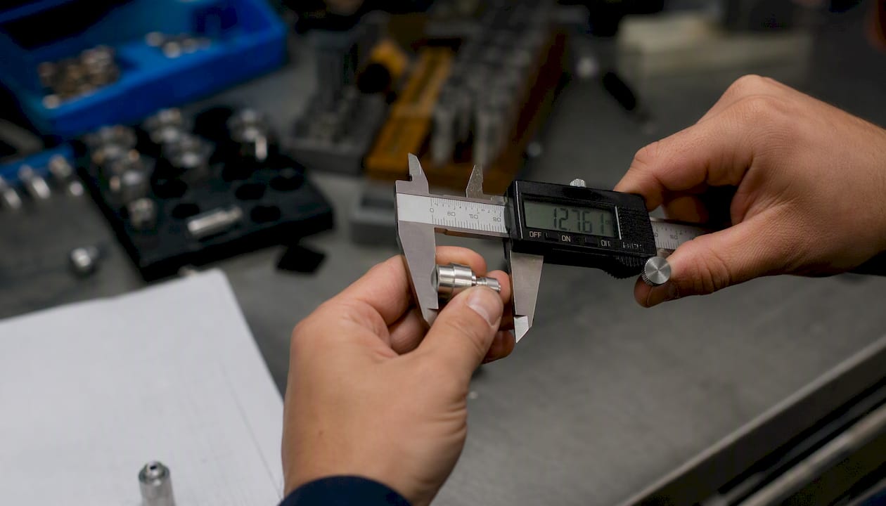 Hands measuring metal part with caliper
